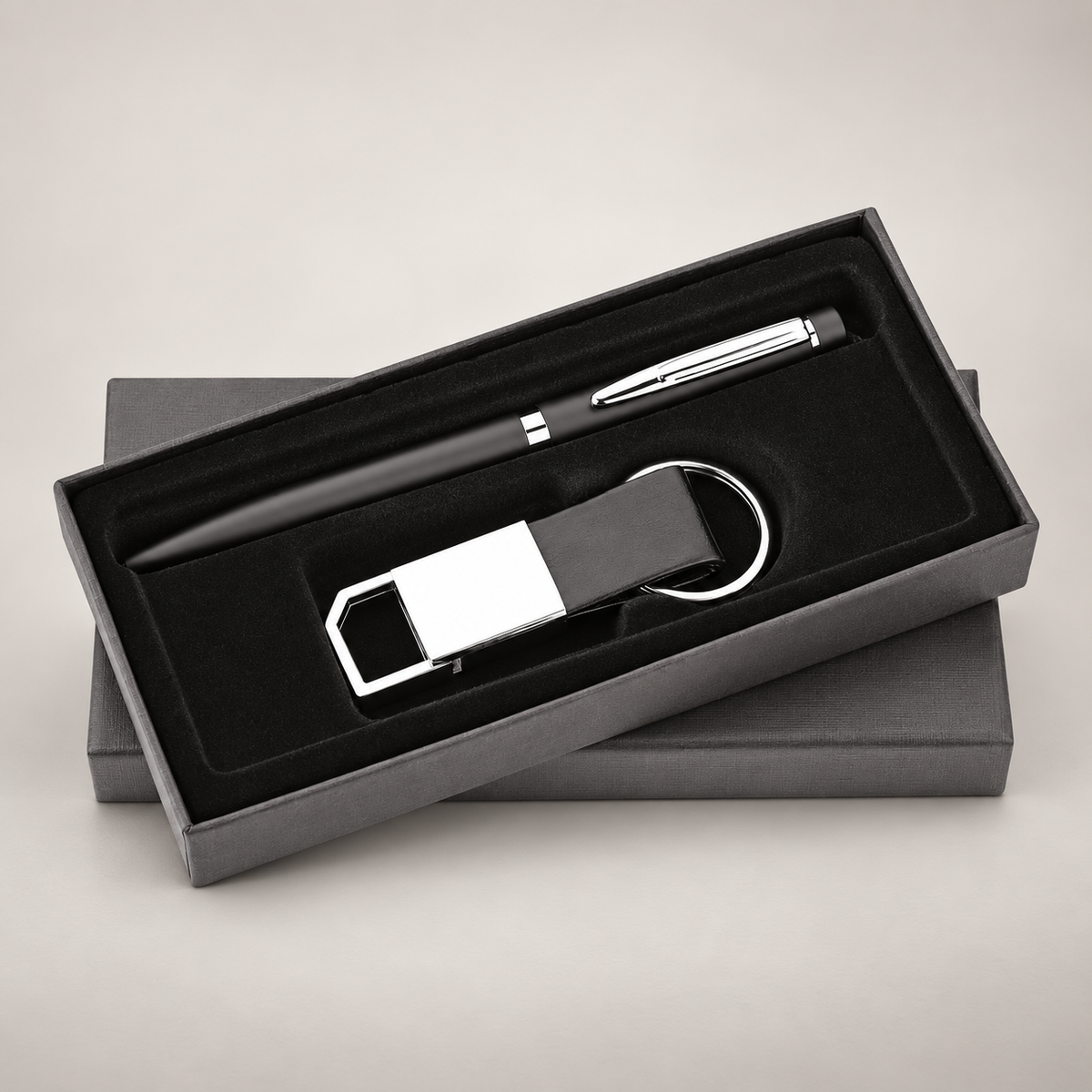 Black pen and rectangular keychain gift set in its presentation box on a warm grey studio background